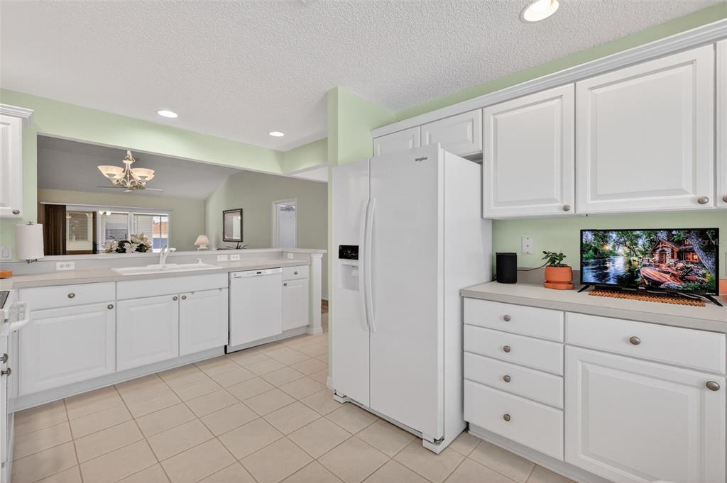 A kitchen features white cabinets, a white refrigerator, and a sink overlooking an adjacent room — 403 MCLEOD LANE, THE VILLAGES, FL