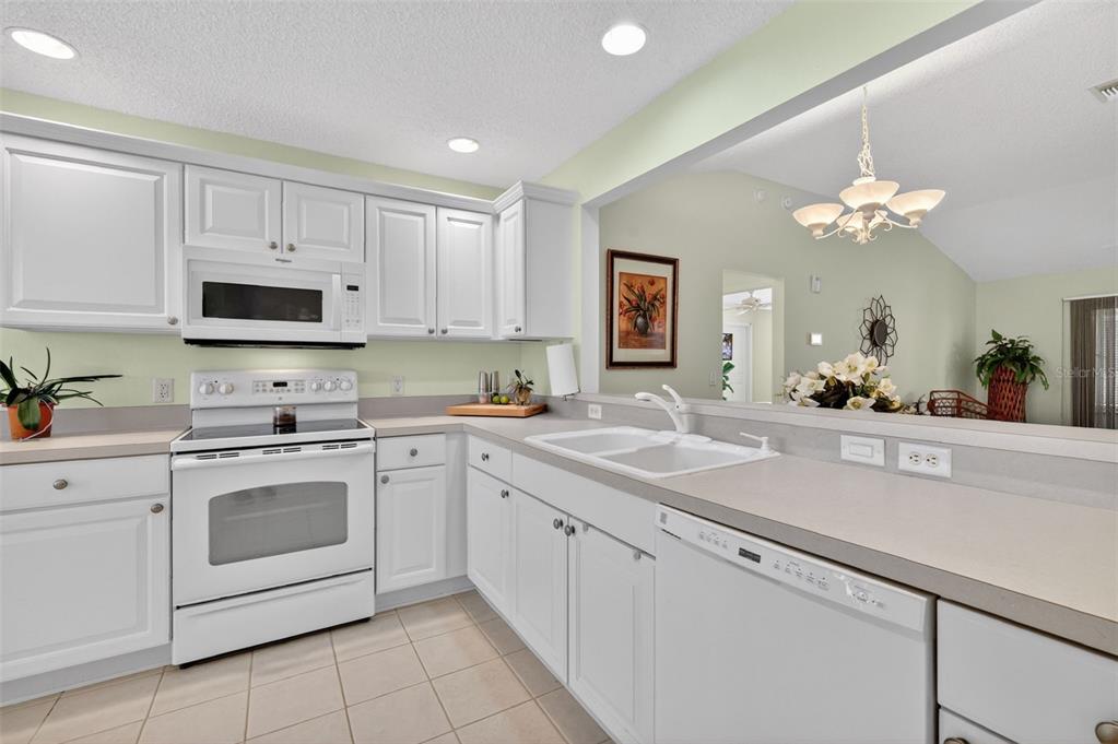 A kitchen with white cabinets, white appliances, and a pass-through window to the living area — 403 MCLEOD LANE, THE VILLAGES, FL