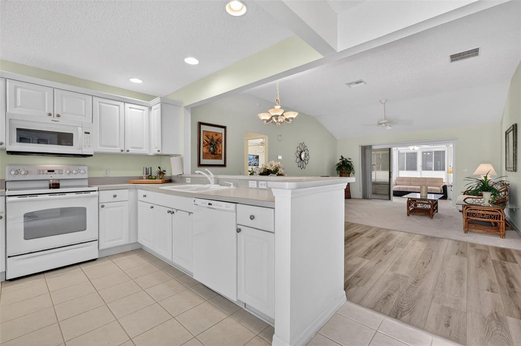 A kitchen with white cabinets and appliances overlooks a living area with wood-look flooring — 403 MCLEOD LANE, THE VILLAGES, FL