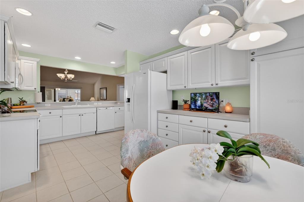 A kitchen features white cabinets, light-colored countertops, tile flooring, and a small dining table — 403 MCLEOD LANE, THE VILLAGES, FL