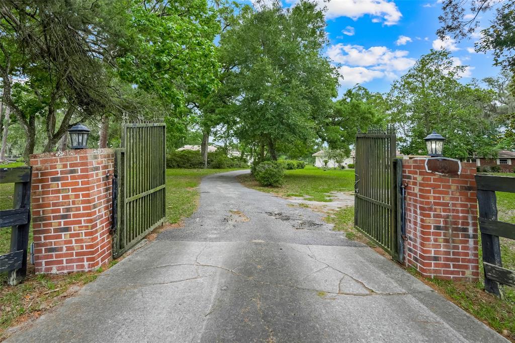 A paved driveway leads through an open metal gate flanked by two brick pillars — 4801 SE HIGHWAY 42, SUMMERFIELD, FL