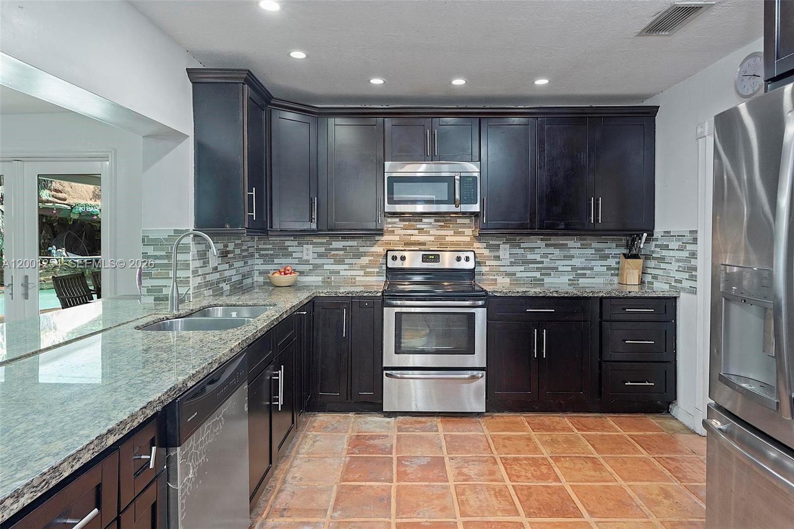 A kitchen features dark wood cabinets, granite countertops, stainless steel appliances, and terracotta tile flooring — 19751 SW 84th Ave, Cutler Bay FL 33189, CUTLER BAY, FL