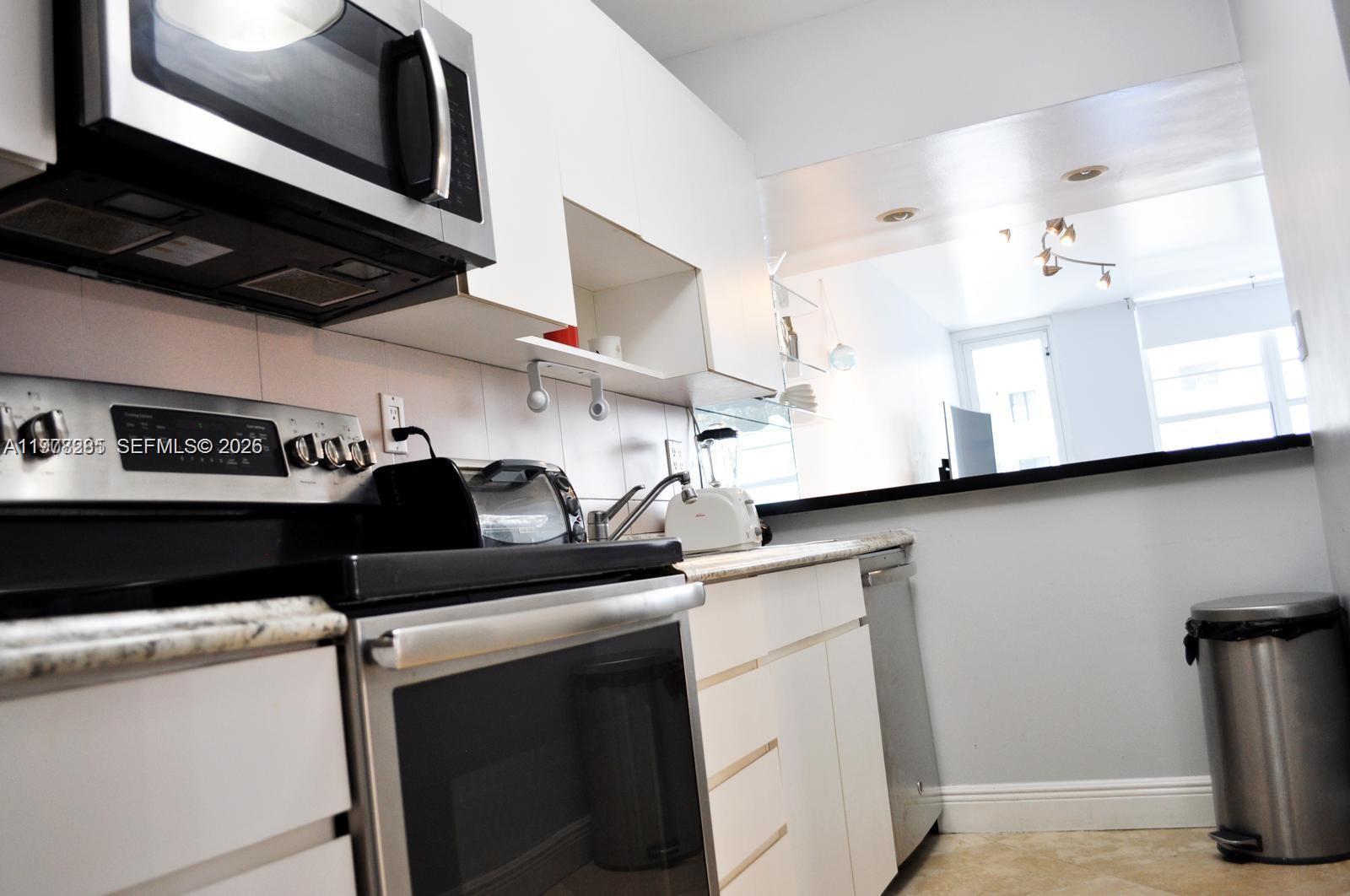 A kitchen features white cabinets, stainless steel appliances, and a pass-through window to another room — 100 Lincoln Rd # 728, Miami Beach FL 33139, MIAMI BEACH, FL