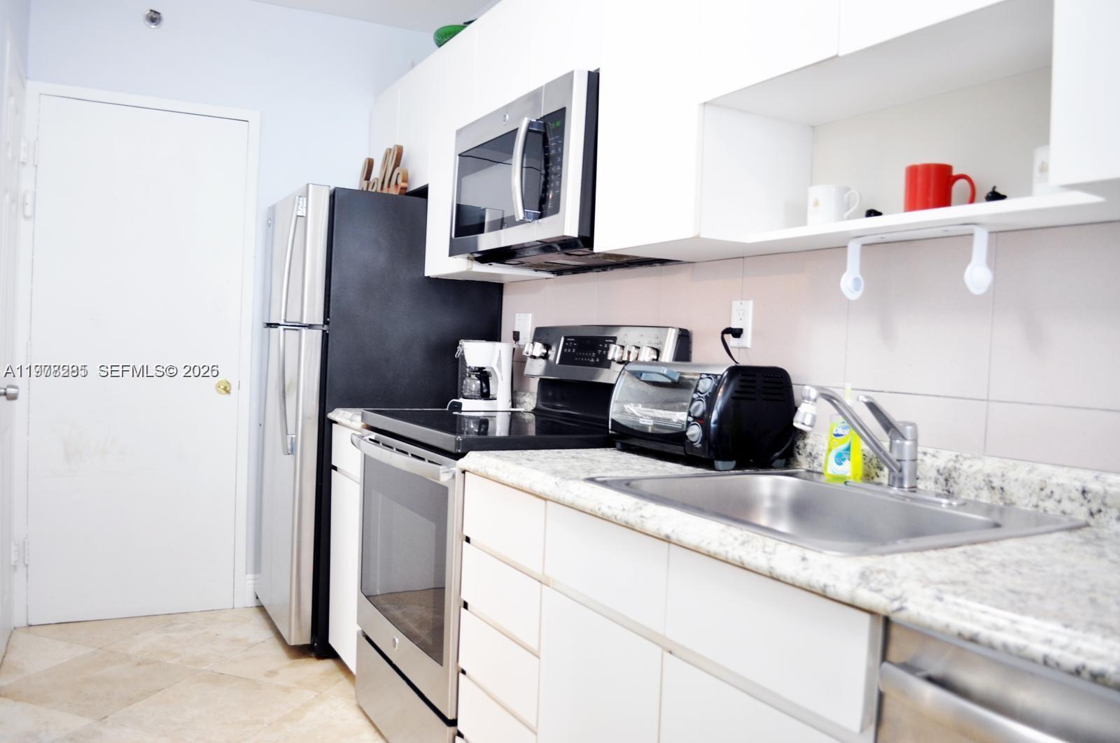 A kitchen features white cabinets, stainless steel appliances, granite countertops, and a stainless steel sink — 100 Lincoln Rd # 728, Miami Beach FL 33139, MIAMI BEACH, FL