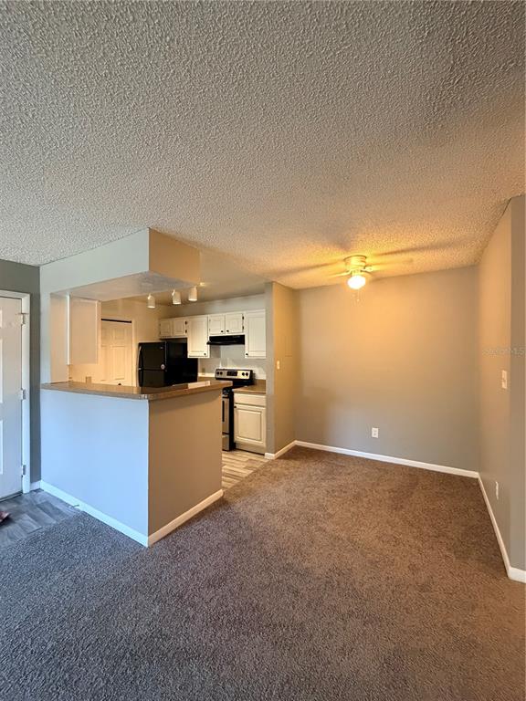 A kitchen with white cabinets and a breakfast bar opens into a carpeted dining area — 4367 THORNBRIAR LANE UNIT 107, ORLANDO, FL