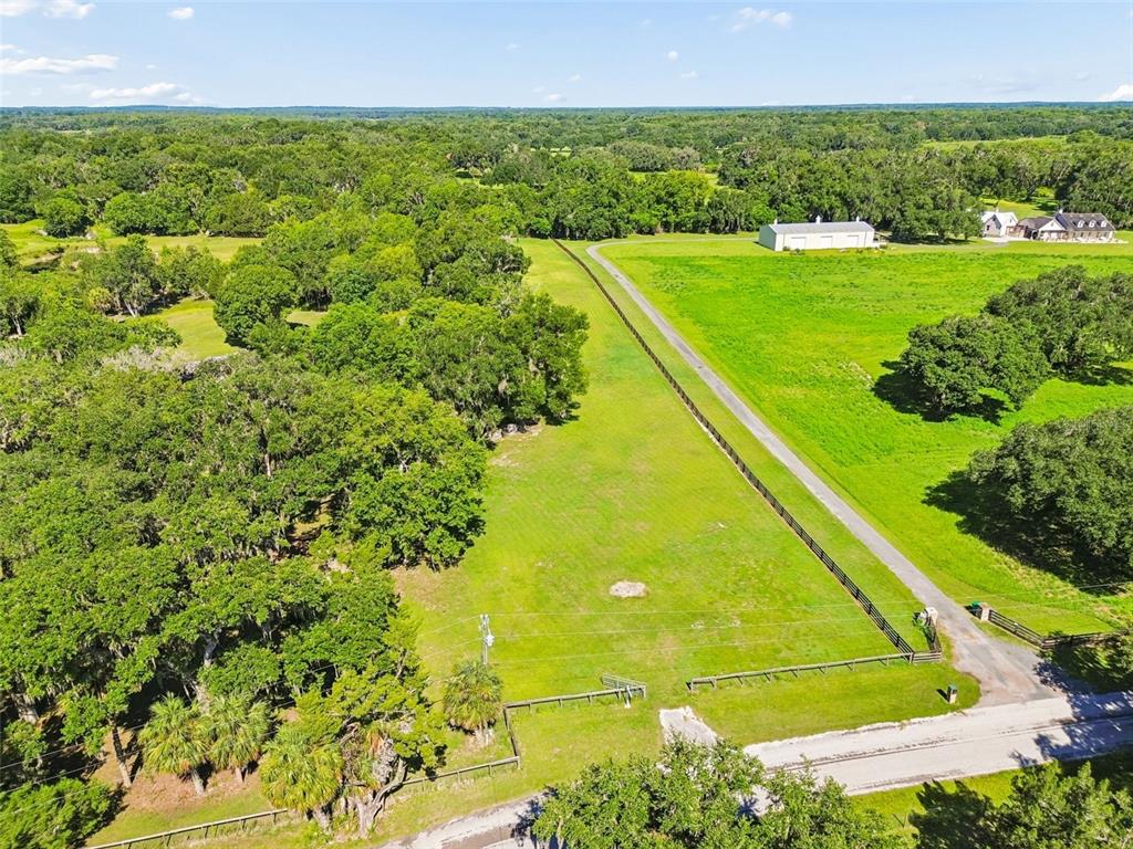 An aerial view shows a fenced pasture bordered by trees and a paved driveway — 8792 S STEED TERRACE, FLORAL CITY, FL