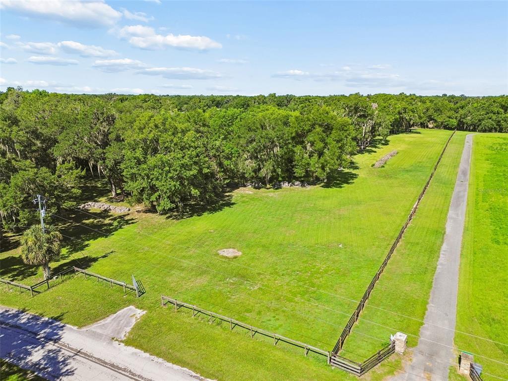 An aerial view shows a fenced grassy lot bordered by trees and a paved driveway — 8792 S STEED TERRACE, FLORAL CITY, FL
