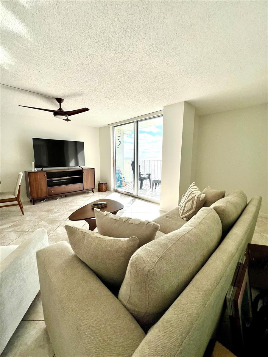 A living room features tile floors, a sofa, a media console, and a balcony view — 111 Briny Avenue # 1908, Pompano Beach FL 33062, POMPANO BEACH, FL
