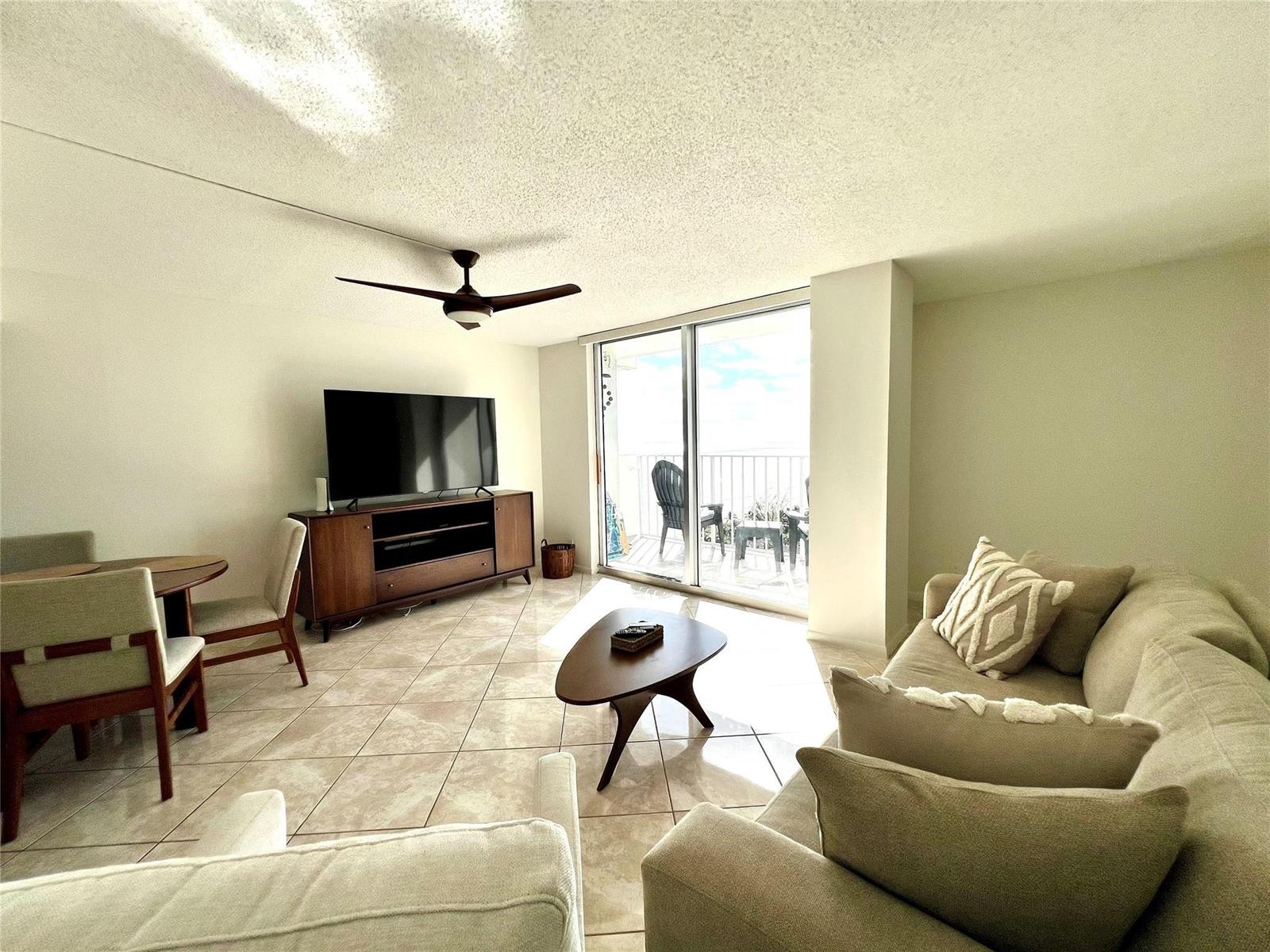 A living room with tile floors, a ceiling fan, a television console, and a balcony — 111 Briny Avenue # 1908, Pompano Beach FL 33062, POMPANO BEACH, FL