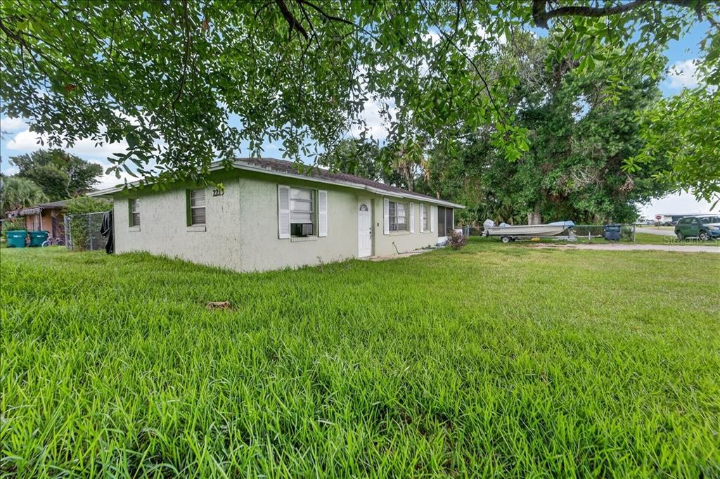 A single-story house with light green stucco siding sits on a large, grassy lot — 2213 NW 3RD STREET, OKEECHOBEE, FL