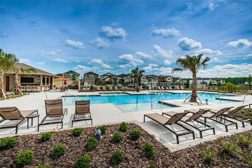 A community swimming pool features lounge chairs, palm trees, and a covered patio area — 8327 CRESCENT OAKS DRIVE, NEW PORT RICHEY, FL