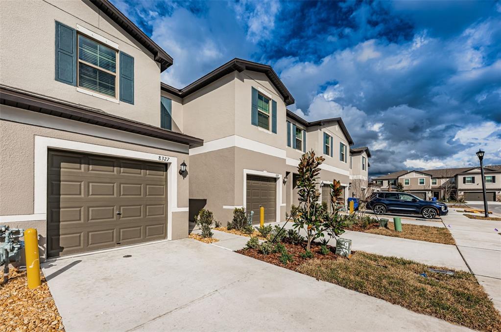 A row of two-story townhouses with beige stucco exteriors, brown garage doors, and blue shutters — 8327 CRESCENT OAKS DRIVE, NEW PORT RICHEY, FL