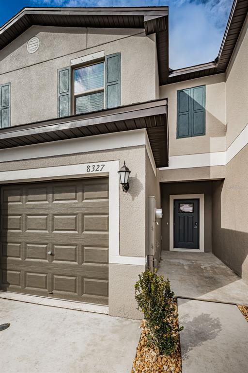A two-story stucco house exterior features a single-car garage, a front door, and dark shutters — 8327 CRESCENT OAKS DRIVE, NEW PORT RICHEY, FL