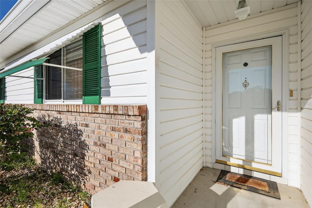A white-sided house exterior features a brick base, green shutters, and a front entry door — 17945 SE 104TH TERRACE, SUMMERFIELD, FL