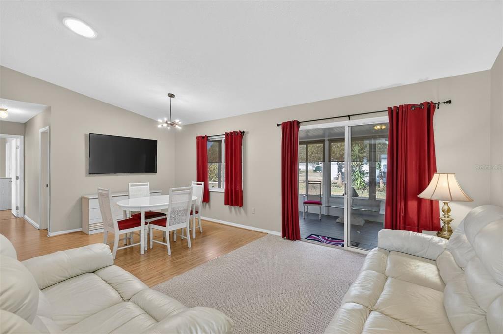 A living and dining room with white leather sofas, wood flooring, and red curtains — 17945 SE 104TH TERRACE, SUMMERFIELD, FL