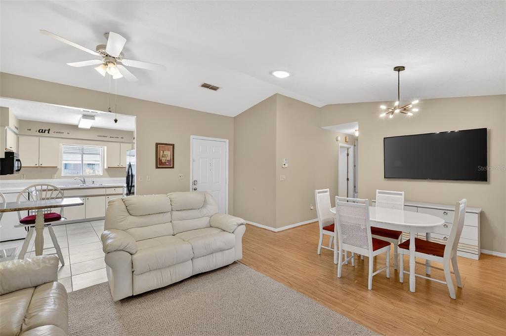 An open-concept living and dining area features light wood flooring, a white sofa, and a television — 17945 SE 104TH TERRACE, SUMMERFIELD, FL