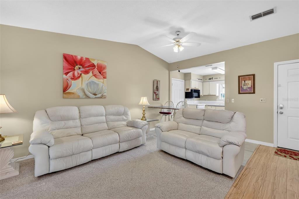 A living room features two white leather sofas, beige walls, and an adjacent kitchen area — 17945 SE 104TH TERRACE, SUMMERFIELD, FL