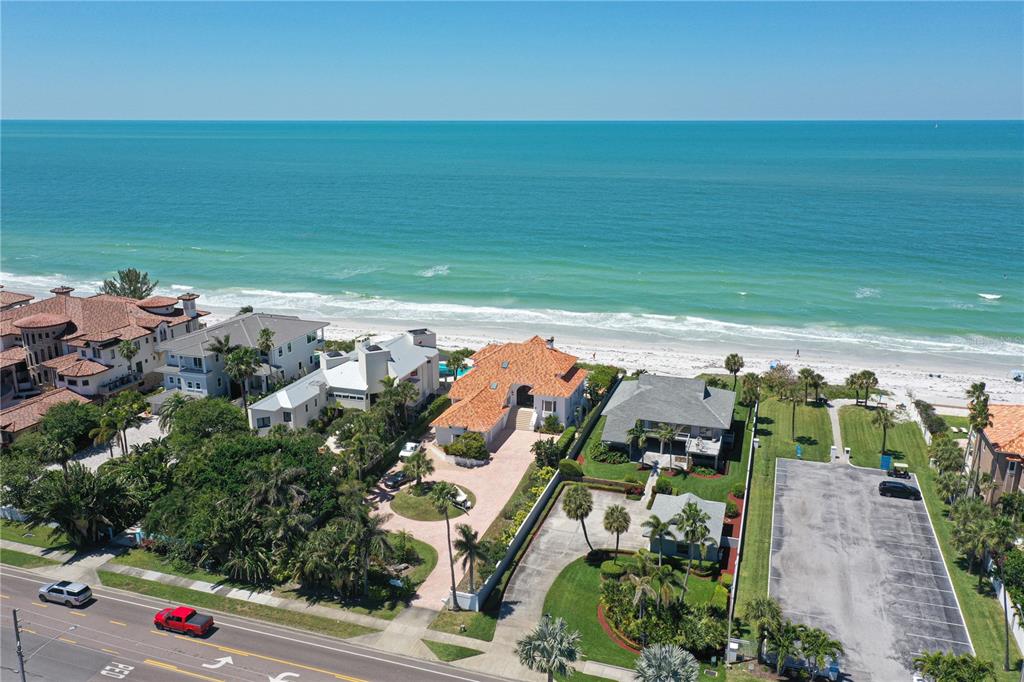 An aerial view shows beachfront houses with tiled roofs, a parking lot, and the ocean — 1800 GULF BOULEVARD, BELLEAIR BEACH, FL
