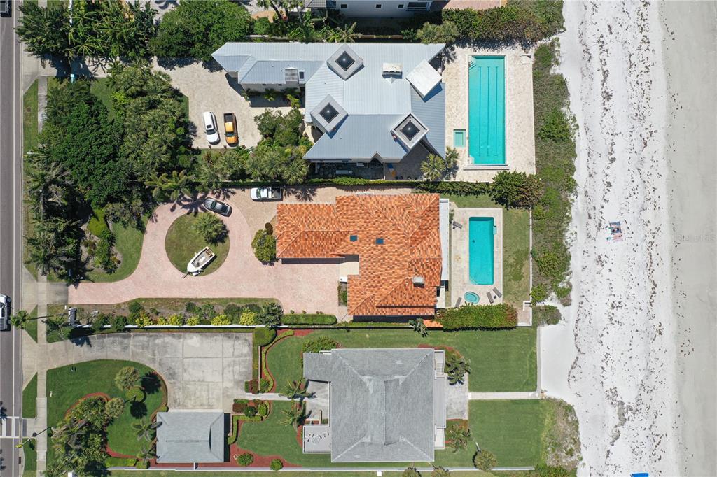 An aerial view shows three beachfront houses with swimming pools, driveways, and landscaped yards — 1800 GULF BOULEVARD, BELLEAIR BEACH, FL