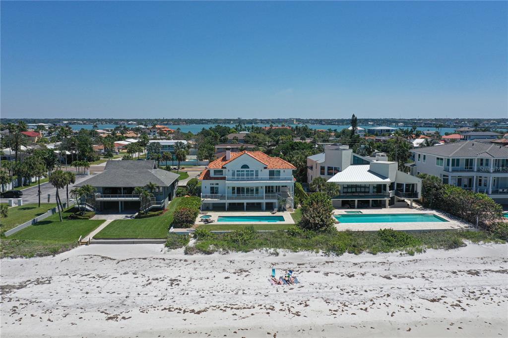 An aerial view shows three beachfront houses with swimming pools along a sandy shore — 1800 GULF BOULEVARD, BELLEAIR BEACH, FL