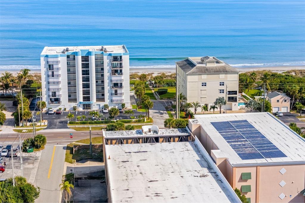 An aerial view shows a multi-story apartment building, a tan building, and a beach — 1900 S. ATLANTIC AVENUE, COCOA BEACH, FL