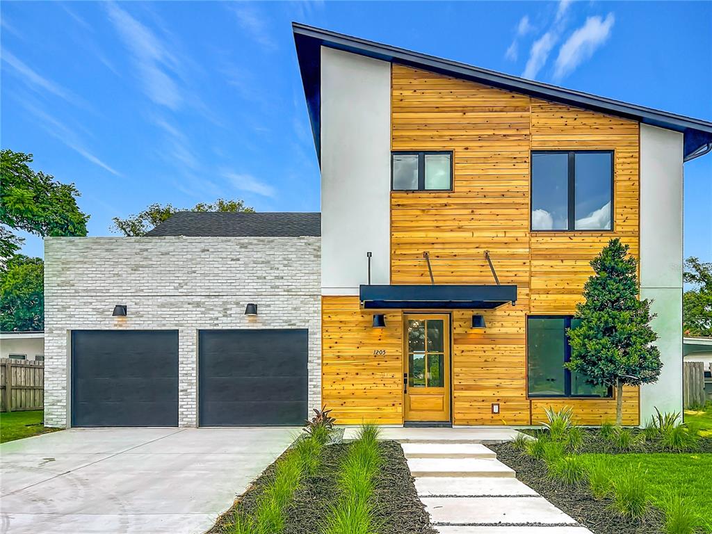A modern two-story house features a wood-paneled facade, white stone garage, and a slanted roof — 1205 FALCON DRIVE, ORLANDO, FL
