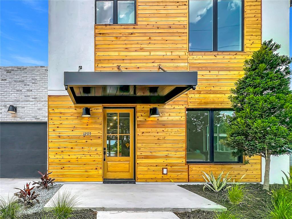 A modern house exterior features horizontal wood siding, a black metal awning, and a glass door — 1205 FALCON DRIVE, ORLANDO, FL