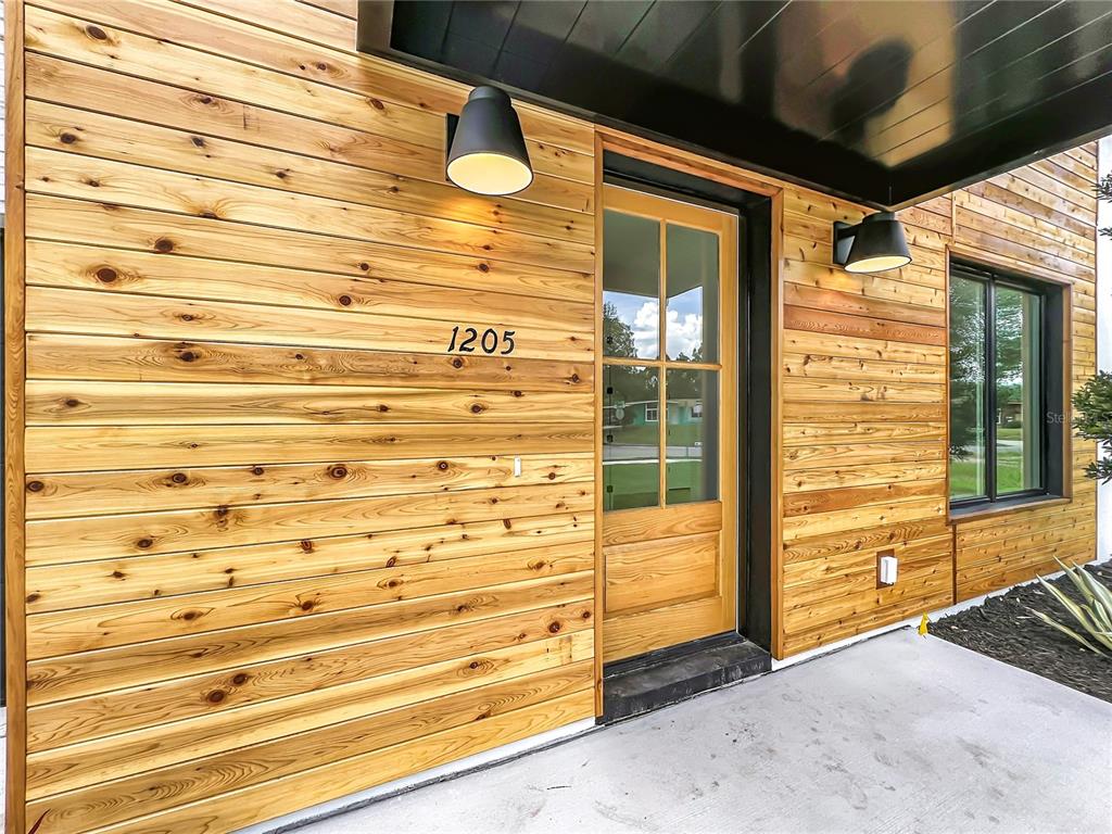 A modern home entrance features horizontal wood siding, a glass-paneled door, and two black sconces — 1205 FALCON DRIVE, ORLANDO, FL
