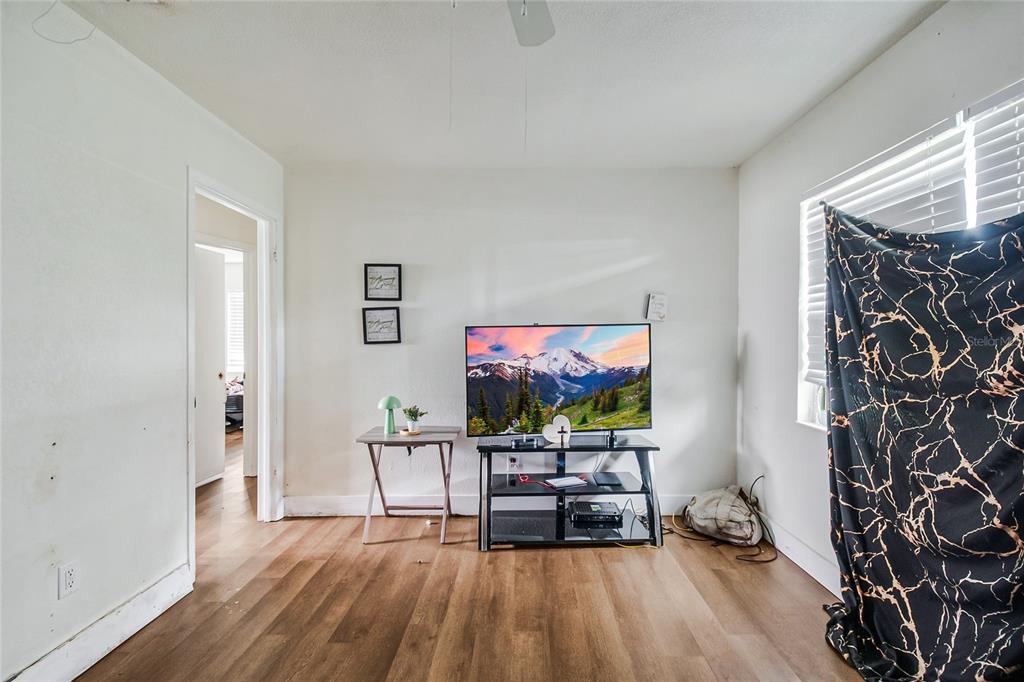 A room with wood-look flooring, a television on a stand, and a window with a curtain — 4135 RALEIGH STREET, ORLANDO, FL