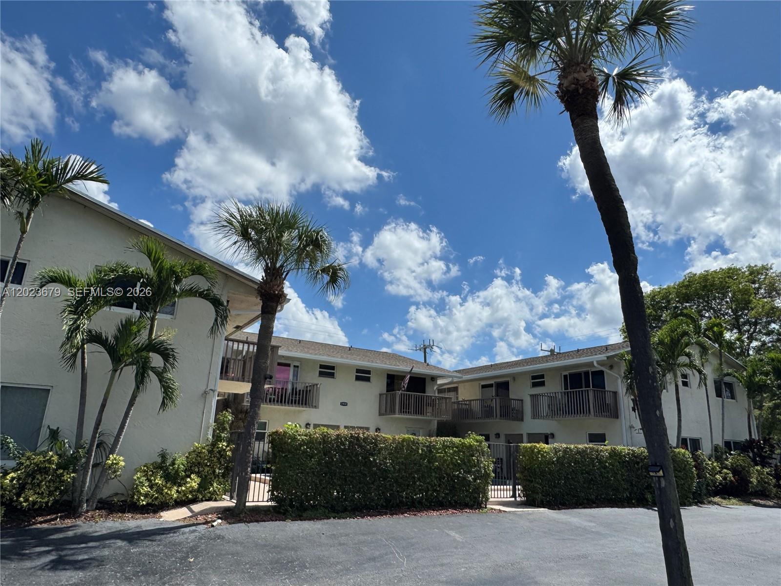 A two-story apartment building with balconies and palm trees under a blue sky — 1910 NE 5th St # 107, Deerfield Beach FL 33441, DEERFIELD BEACH, FL