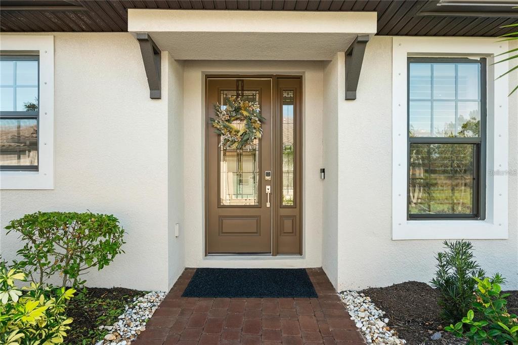 A brown front door with a glass insert and wreath sits under a covered entryway — 15672 SACILE LANE, BRADENTON, FL