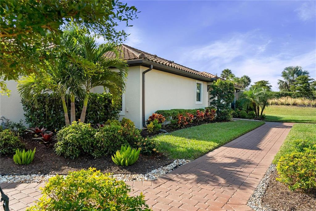 A paved walkway leads along the side of a house with landscaping and palm trees — 15672 SACILE LANE, BRADENTON, FL