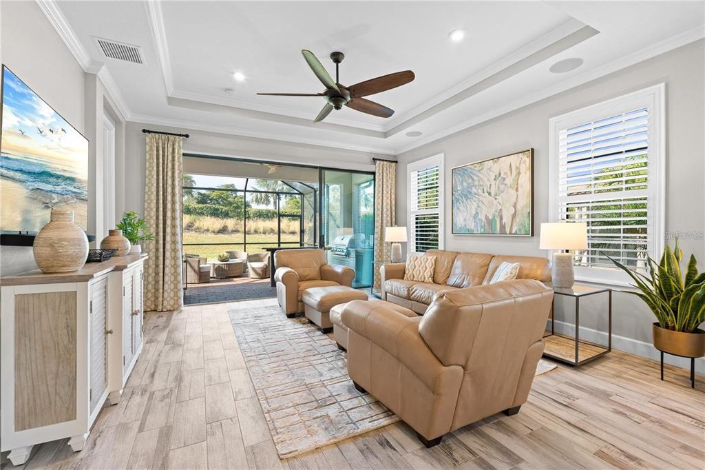 A living room with tan leather furniture, a tray ceiling, and sliding doors to a patio — 15672 SACILE LANE, BRADENTON, FL