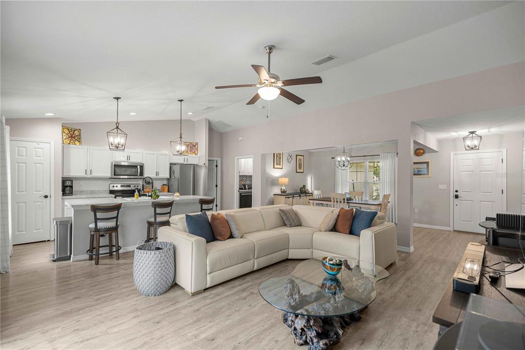 An open-concept living room and kitchen featuring a sectional sofa, island seating, and light flooring — 19855 SW 59TH LANE, DUNNELLON, FL