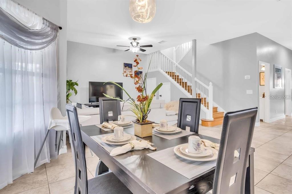 A dining area with a dark table and chairs sits in front of a living room and staircase — 241 VISTA LOOP, DAVENPORT, FL
