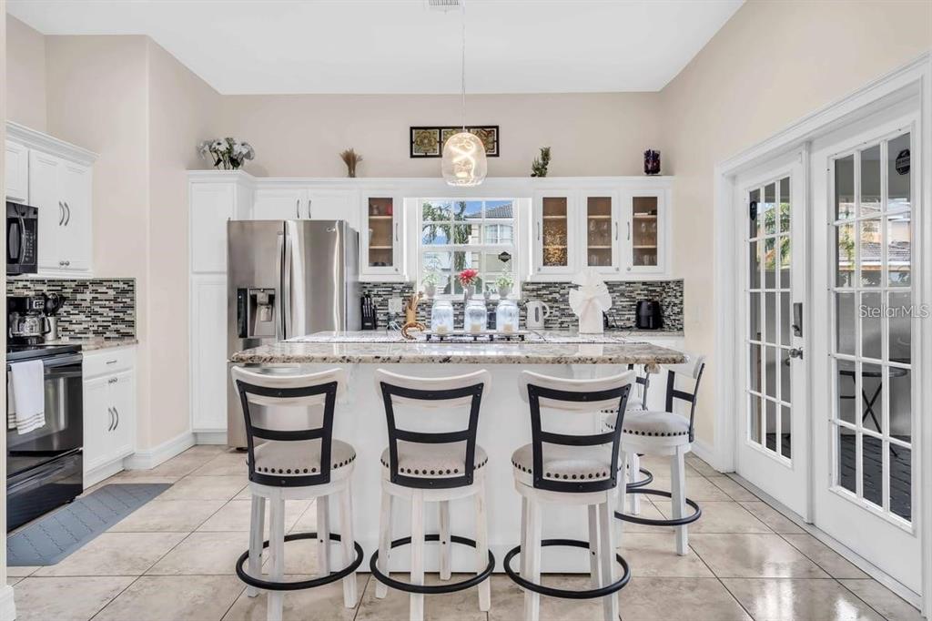 A kitchen features white cabinets, granite countertops, a central island with three stools, and tile flooring — 241 VISTA LOOP, DAVENPORT, FL