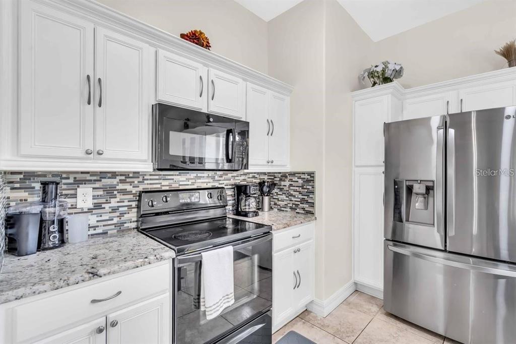 A kitchen features white cabinets, granite countertops, stainless steel appliances, and a mosaic tile backsplash — 241 VISTA LOOP, DAVENPORT, FL