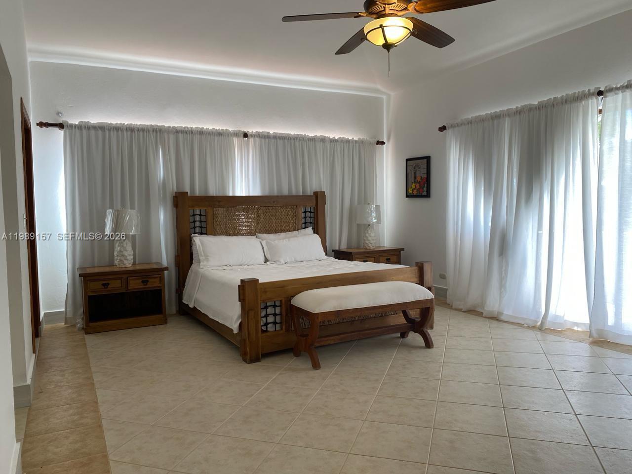A bedroom features a wooden bed frame, tile flooring, and white curtains covering the walls — La Canada Town Home 10B (TH10B), FL
