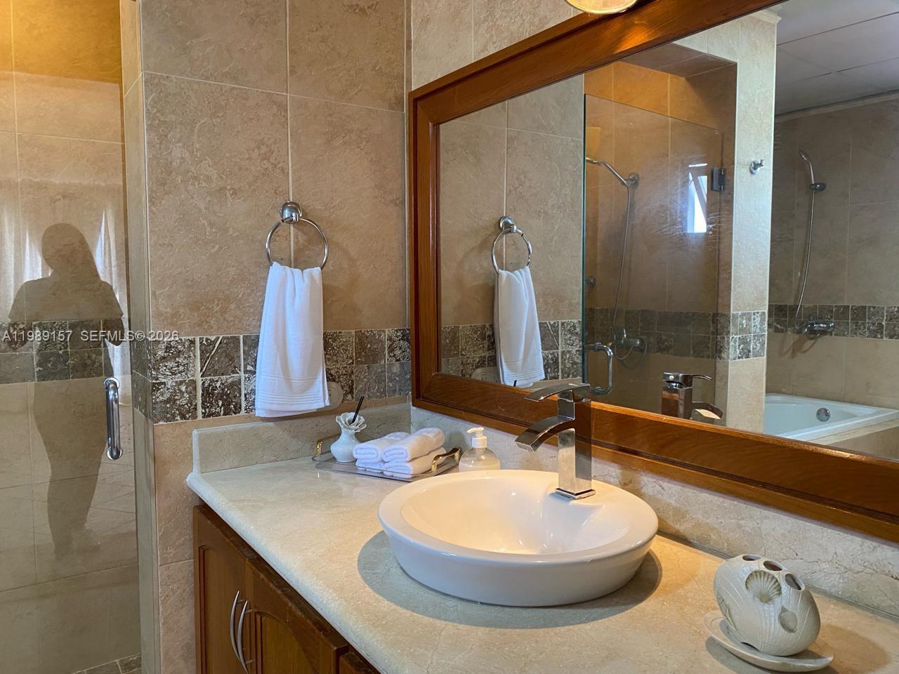 A bathroom features a vessel sink, a wooden-framed mirror, and beige tiled walls — La Canada Town Home 10B (TH10B), FL