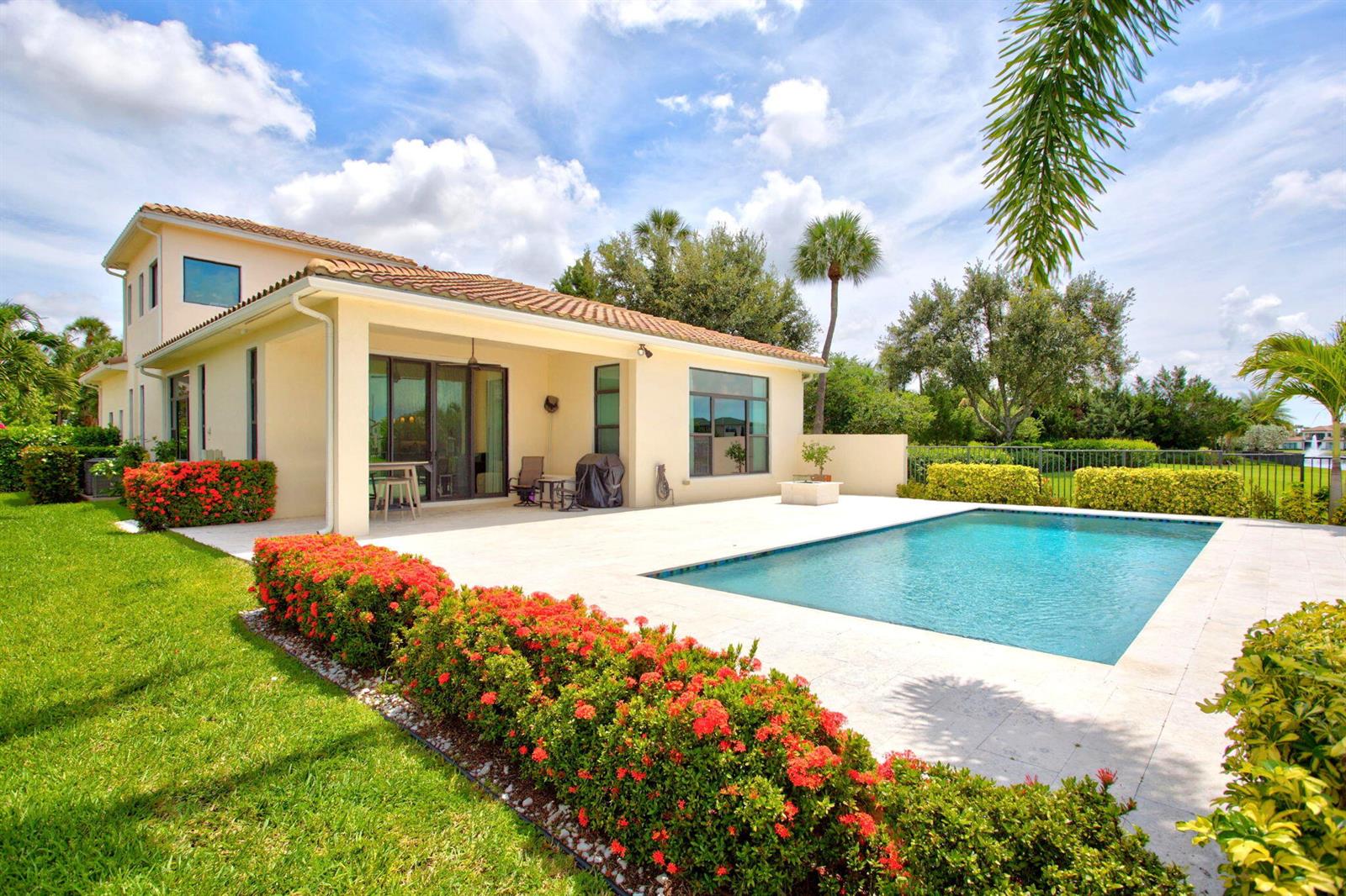 A backyard features a swimming pool, a covered patio, and vibrant red flowering bushes — 8236 Grand Prix Lane, Boynton Beach FL 33472, BOYNTON BEACH, FL