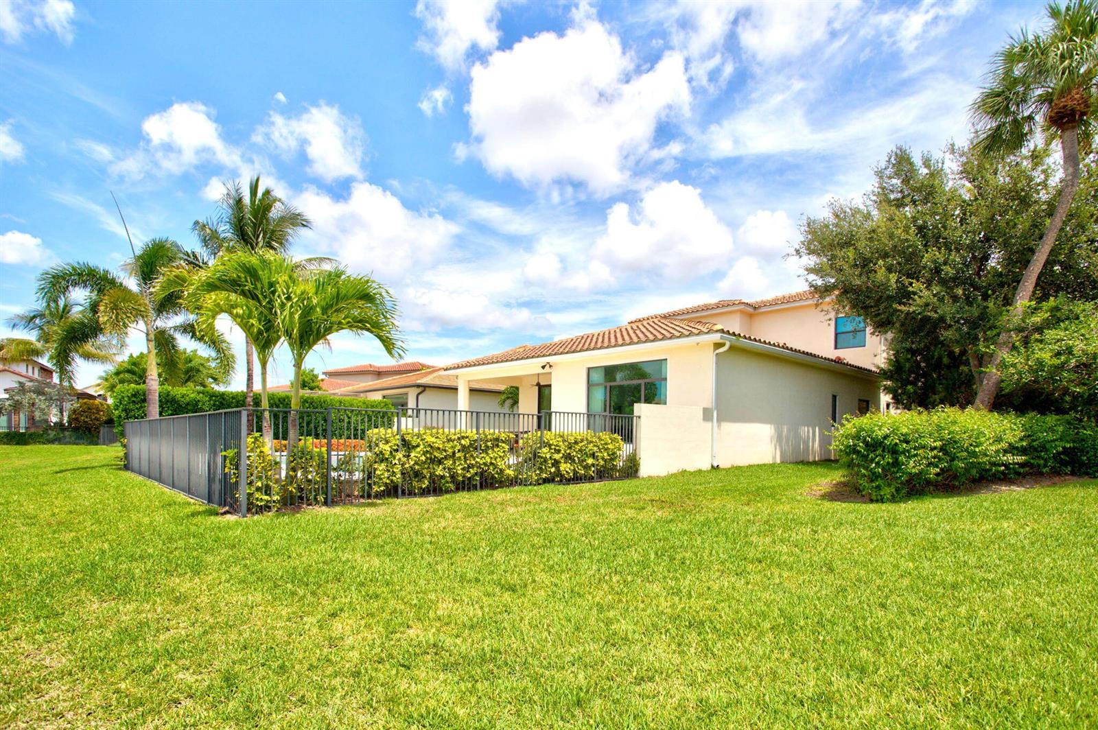 A fenced backyard with a lawn, palm trees, and a beige house with a patio — 8236 Grand Prix Lane, Boynton Beach FL 33472, BOYNTON BEACH, FL