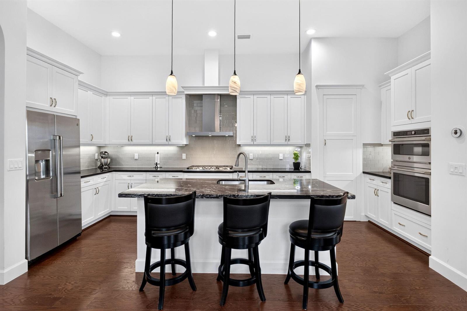 A modern kitchen features white cabinetry, dark granite countertops, a central island, and stainless appliances — 8236 Grand Prix Lane, Boynton Beach FL 33472, BOYNTON BEACH, FL