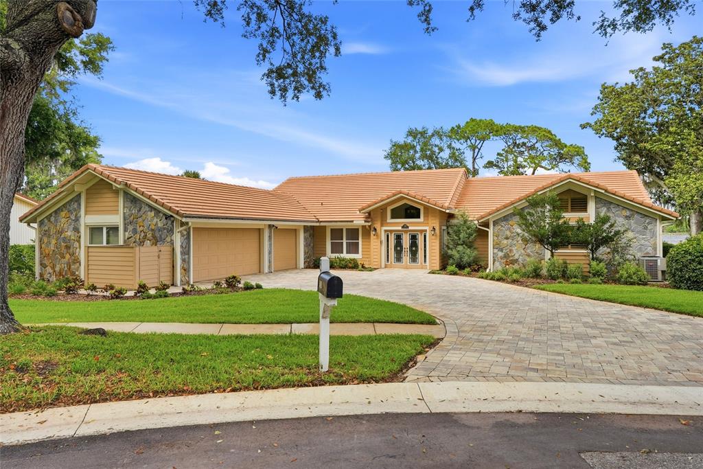 A single-story house with a stone facade, tan siding, a tile roof, and a paved driveway — 3493 SHORELINE CIRCLE, PALM HARBOR, FL
