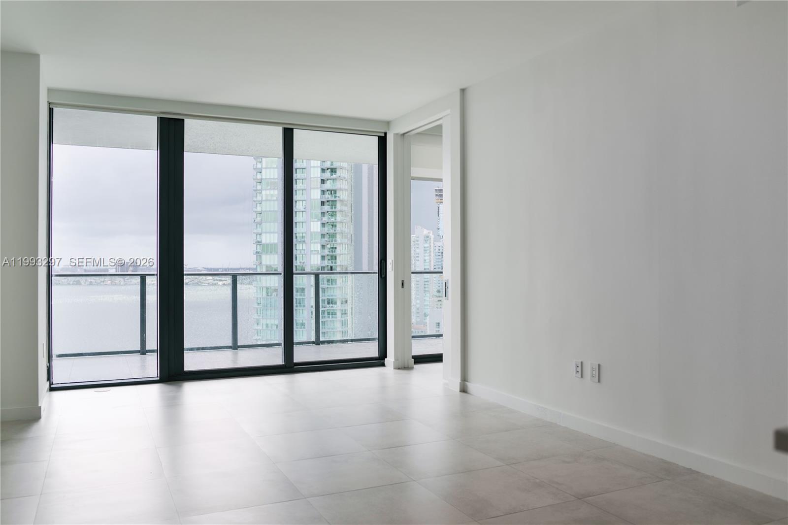 An empty room with large floor-to-ceiling windows, light tile flooring, and a balcony view — 650 NE 32nd St # 2104, Miami FL 33137, MIAMI, FL