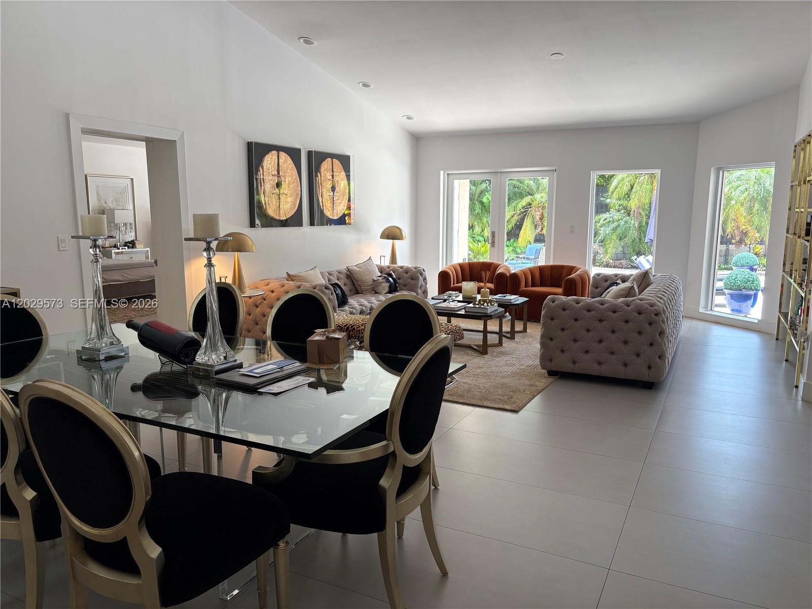 A bright, open-concept living and dining area features tufted sofas, black chairs, and glass tables — KEY BISCAYNE, FL