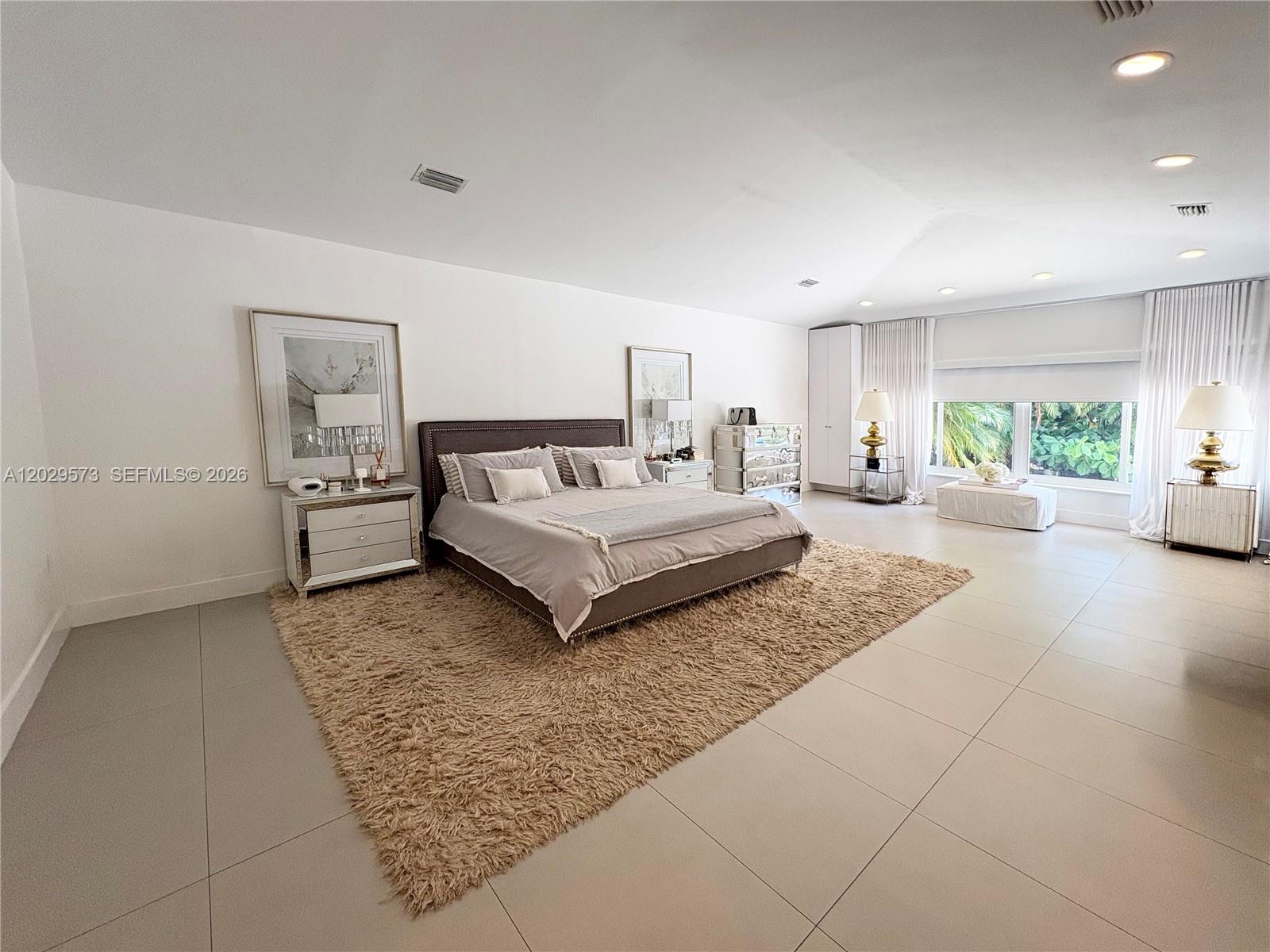 A spacious bedroom features a large bed on a shaggy rug and tiled flooring — KEY BISCAYNE, FL