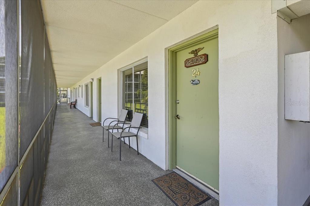 A long, covered outdoor walkway features a green door labeled 24 and two metal chairs — 1700 6TH ST NW UNIT C24, WINTER HAVEN, FL