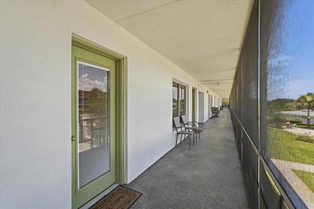 A long, covered outdoor balcony features a green door, concrete flooring, and screened-in walls — 1700 6TH ST NW UNIT C24, WINTER HAVEN, FL