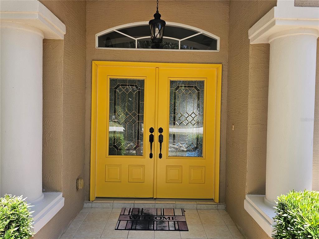 A bright yellow double front door with glass inserts sits between two white columns — 34224 SHADEWOOD CIRCLE, LEESBURG, FL