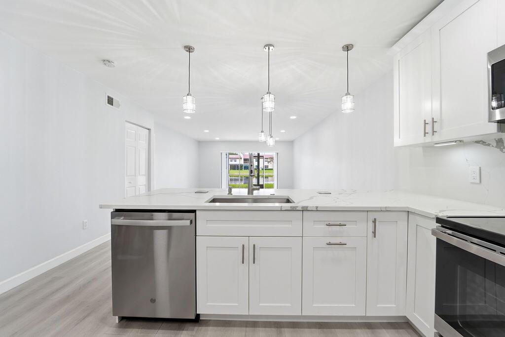 A modern kitchen features white cabinets, a quartz countertop island, and stainless steel appliances — 21839 Arriba # 10g, Boca Raton FL 33433, BOCA RATON, FL